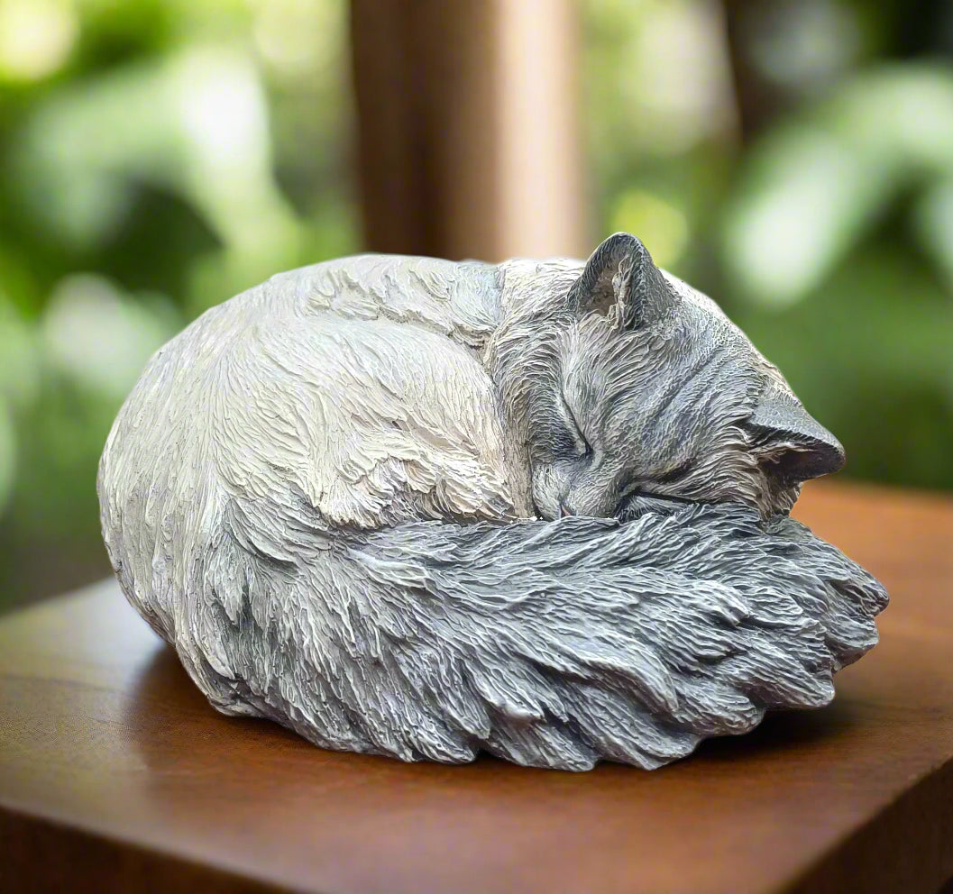 Statue of a sleeping cat on a wooden surface with a blurred green background